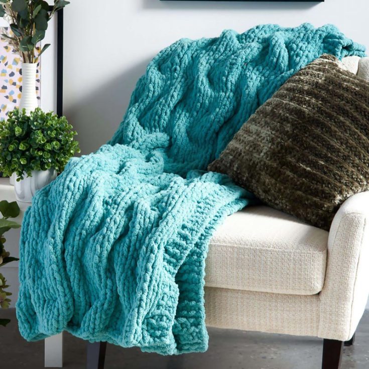 Knit a simple blanket that is so chunky, squishy, and plushy to cuddle in during those cold, chilly nights by the fireplace! This blanket combines the softness of the super chunky yarn and features a captivating tuck stitch pattern with elegant shadow cables. It&rsquo;s a beginner pattern, making it ideal for knitters of all skill levels to try, and this piece promises warmth and style for any cozy corner of your home. The finished measurements are 48&rdquo; x 60&rdquo;.