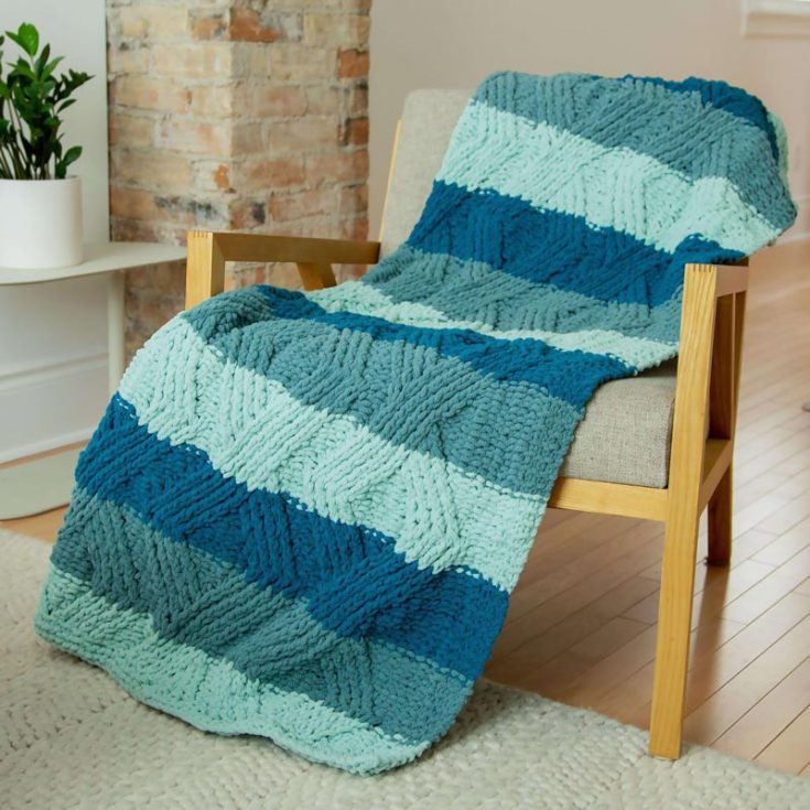Speaking of simple and classic, this Twisted Stitch Blanket is a delightfully textured masterpiece that adds the perfect amount of warmth to snuggle in! Not to mention, it will look fantastic draped over a couch. This intermediate design is knitted with Bernat Softee Chunky yarn in vintage white, and it offers a modern twist to the traditional cable knit design! Just click the link below, and the PDF guide will teach you everything you need to know to replicate this gorgeous piece filled with striking geometric cable motifs. The finished size is 56&rdquo; x 60&rdquo;.