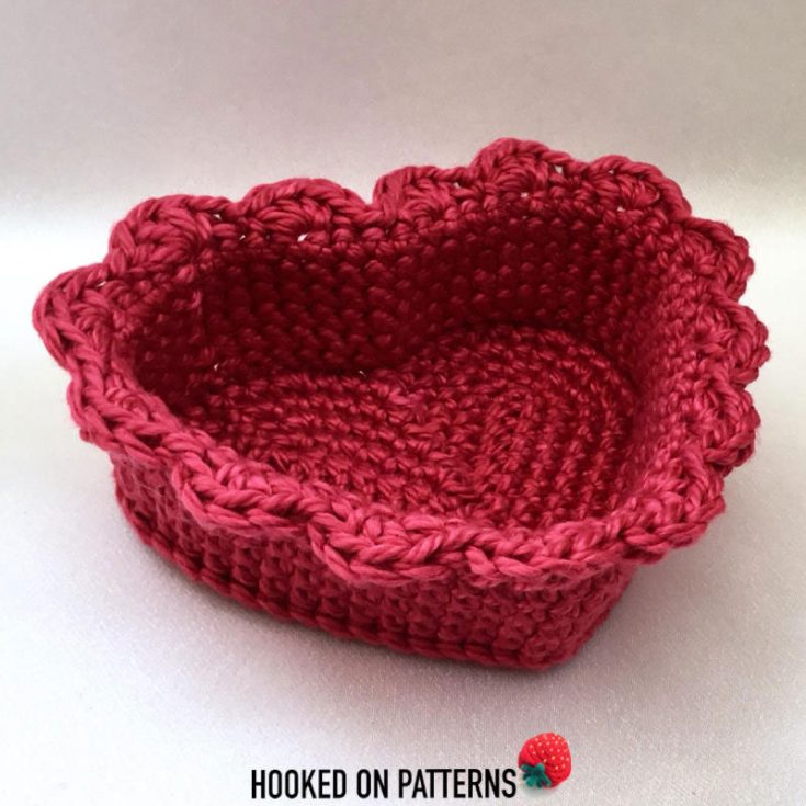 Crochet a charming heart basket starting with a sturdy heart-shaped base. The sides are worked up seamlessly. The basket is finished with delicate shell edging for a decorative touch.